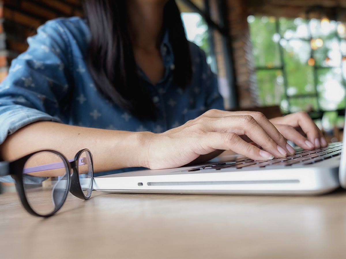 woman typing on laptop with glasses next to her